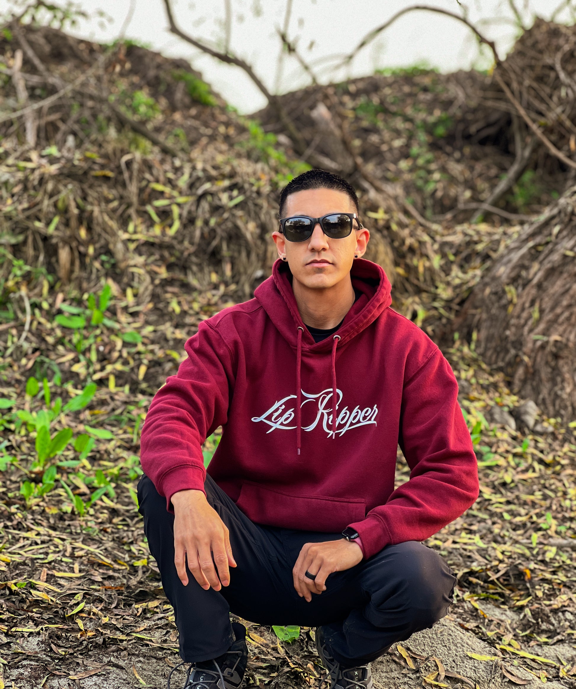 Person with sun glasses on by a river with a burgundy hoodie that says Lip Ripper